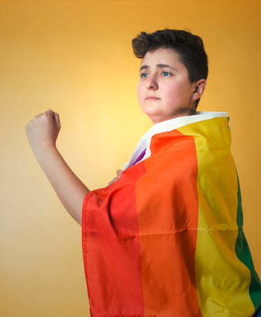 person draped in pride flag gazing into a bright future