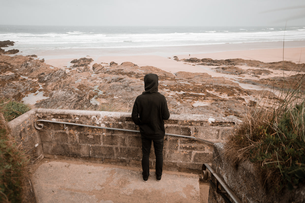 person dressed in black looks out to a sandy beach