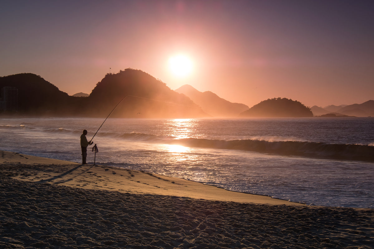 日落时在海滩上钓鱼的人的剪影