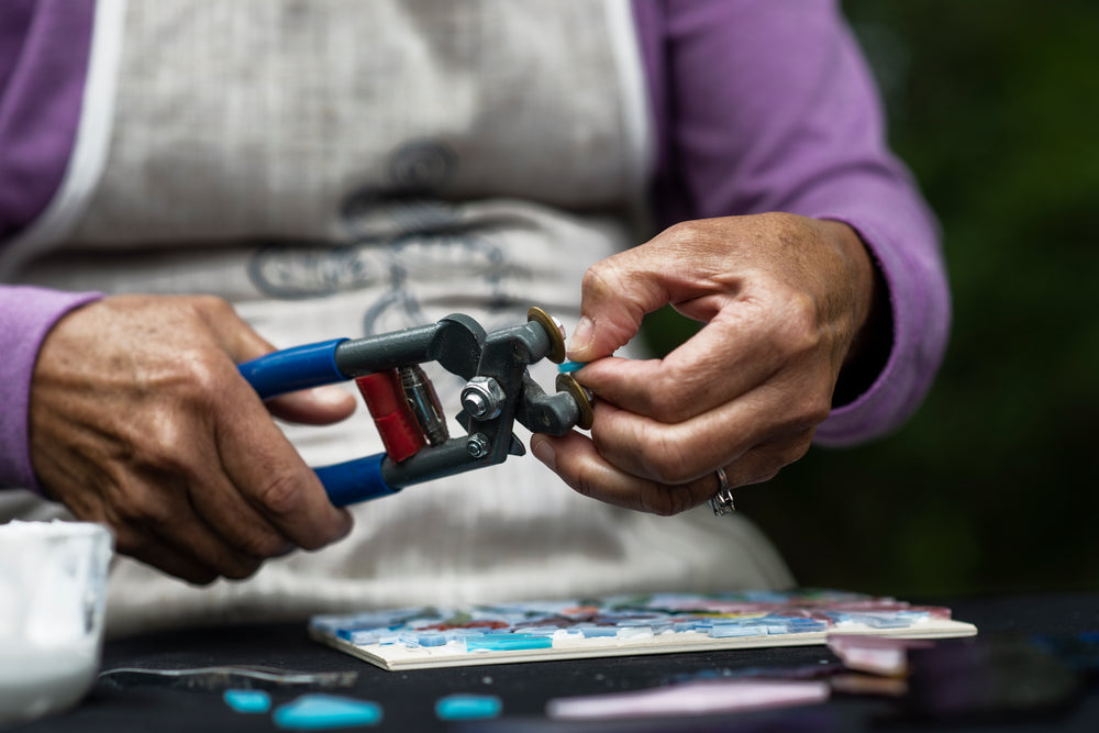 person grips glass cutters to trim a small piece of blue glass