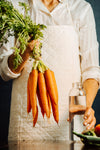person holds a glass bottle and carrots by their tops
