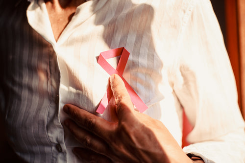 person holds a pink ribbon to their chest