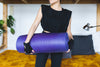person holds a rolled up yoga mat under arm