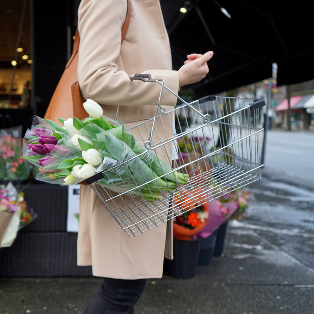 person holds a shopping basket with purple and white tulips