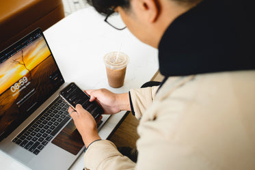 person holds cell phone with both hands over a laptop