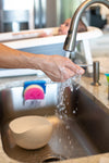 person holds hand under running water in kitchen