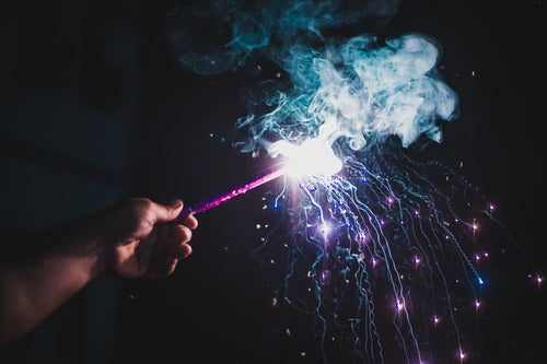 person holds lit firework with purple smoke