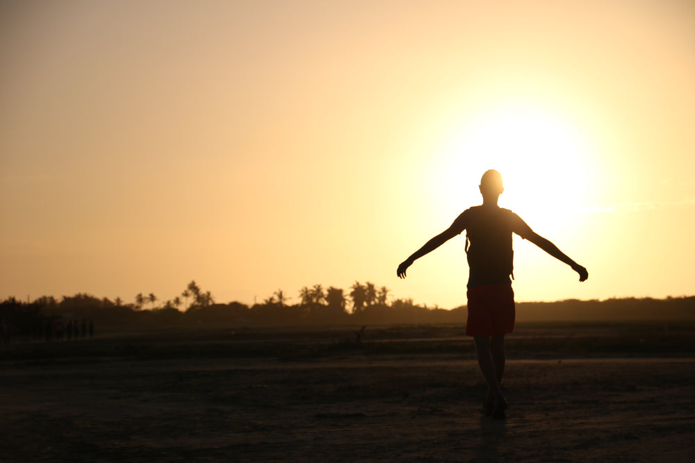 person holds out arms silhouetted by a setting sun