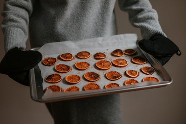 person holds silver baking tray filled with baked oranges