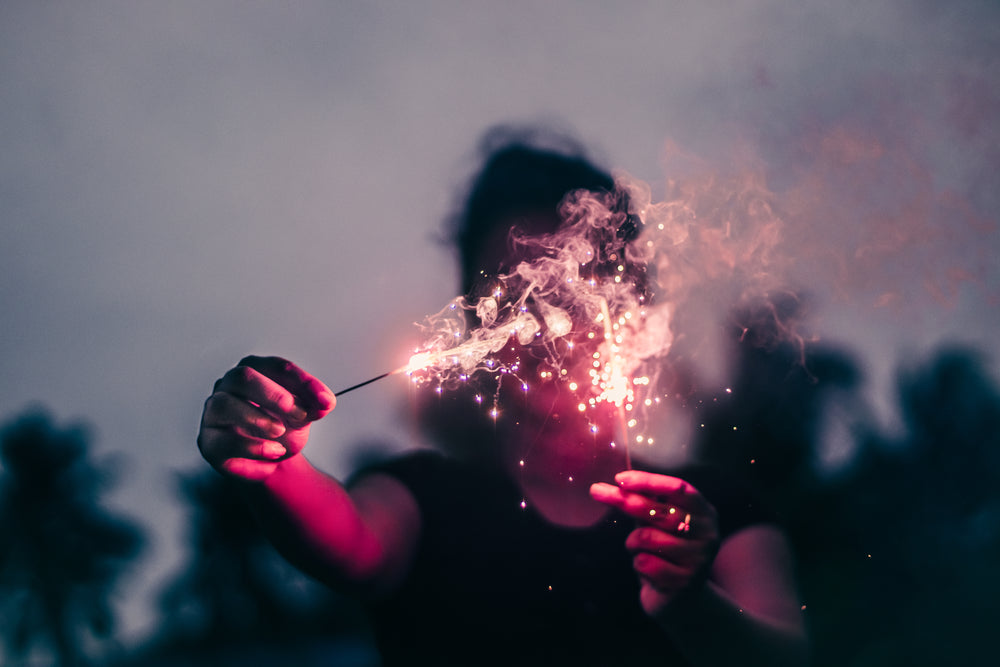 person holds sparklers out blocking their face