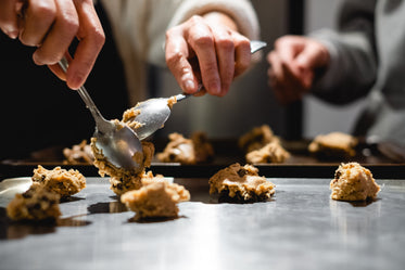 person holds spoons to portion cookie dough to cook