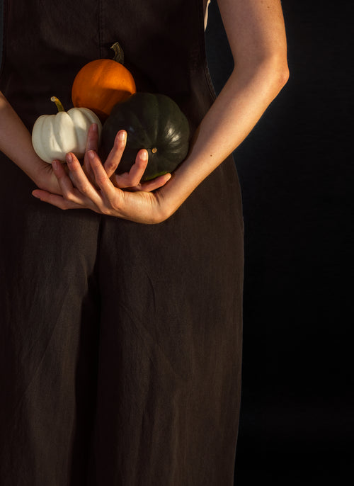 person holds three ting pumpkins behind their back