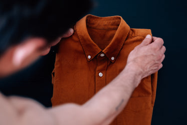 person holds up an orange dress shirt