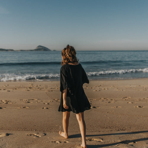 Person In A Black Dress Walks On The Beach