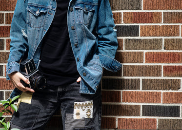 person in a blue jean jacket leans against a red brick wall