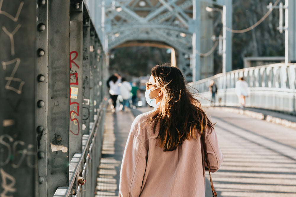 person in a face mask strolls across a bridge