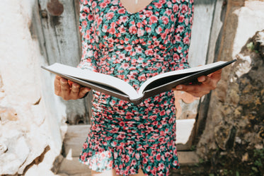 person in a floral dress holds a large book open