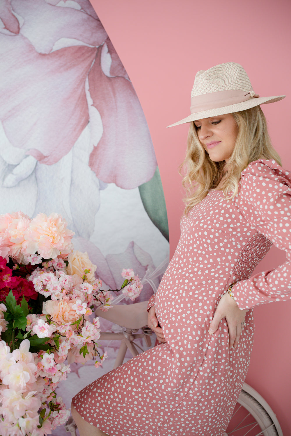 person in a pink dress and a hat holds there belly