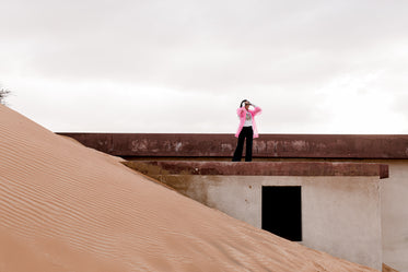 person in a pink jacket stands on sand covered building