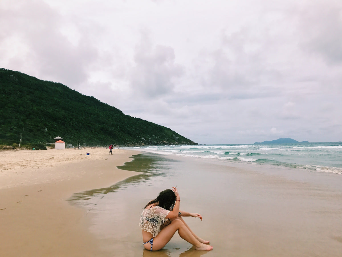 person in a swimsuit sits on a wet sandy beach
