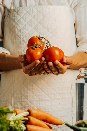 person in a white apron cups a tomatoes