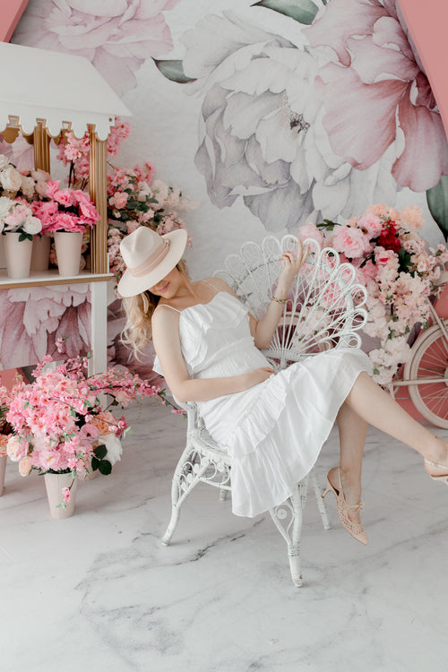 person in a white dress and hat sits in a floral room