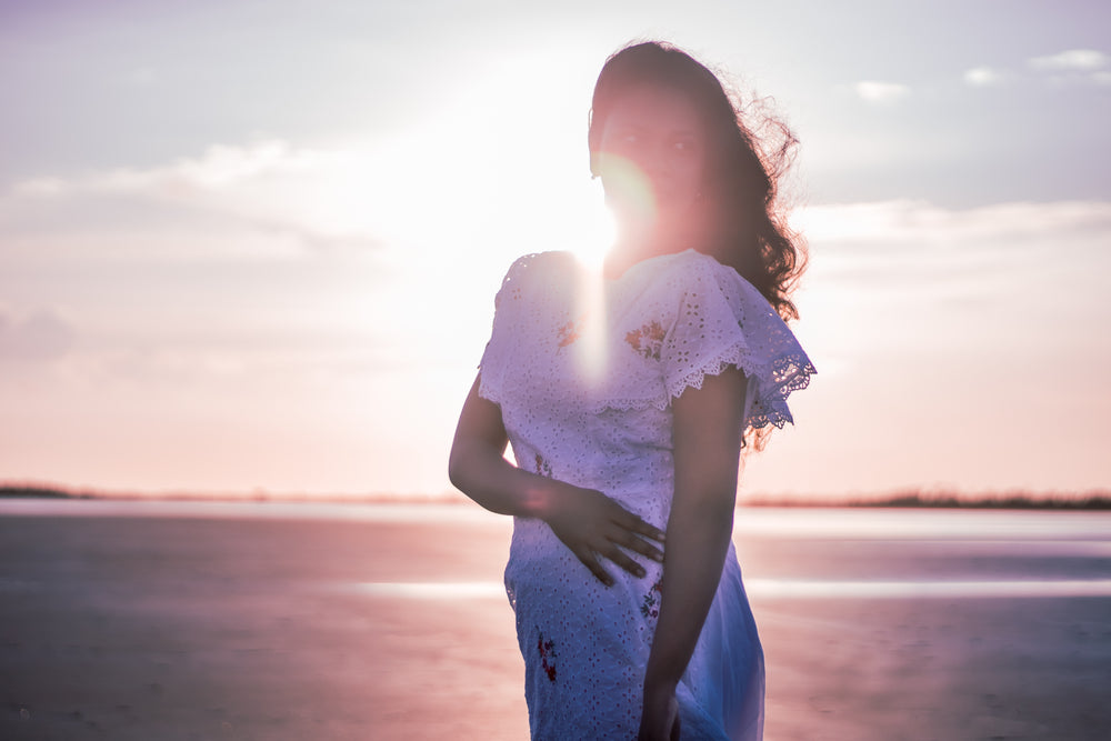 person in a white dress stands on the beach at sunset