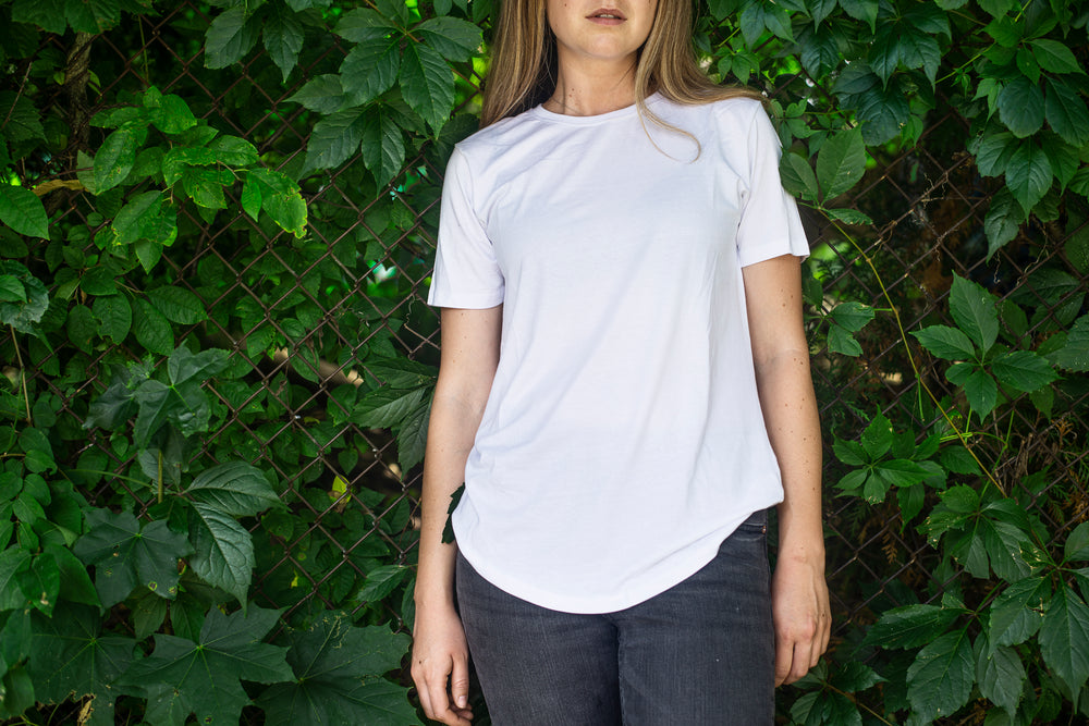 person in a white shirt leaning against a vine covered fence