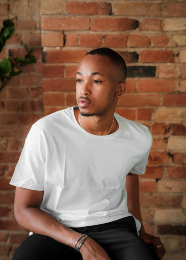 person in a white t shirt looks left against brick wall