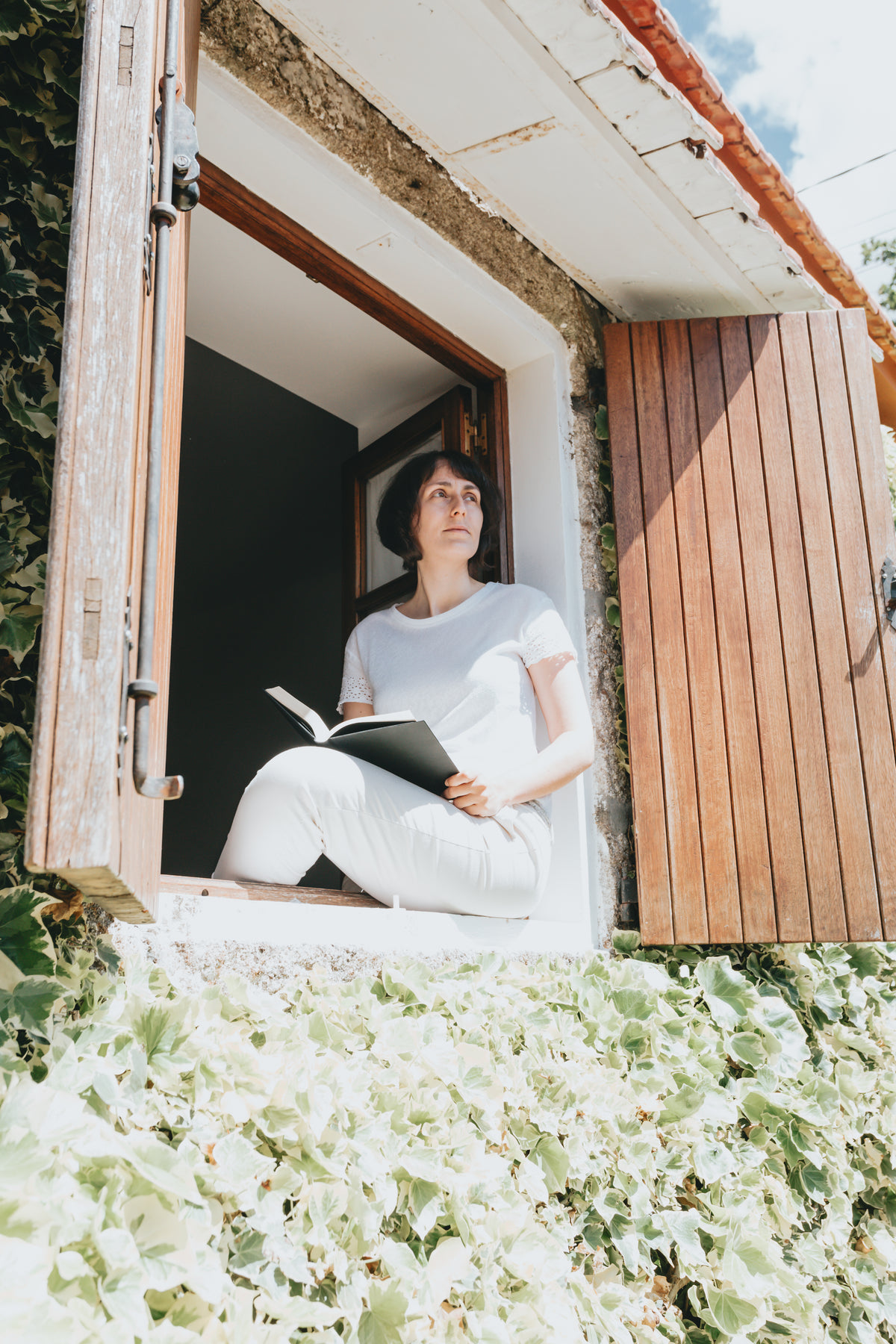person in all white reads a book sitting in a window