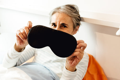 person in bed holds their eye mask for the camera