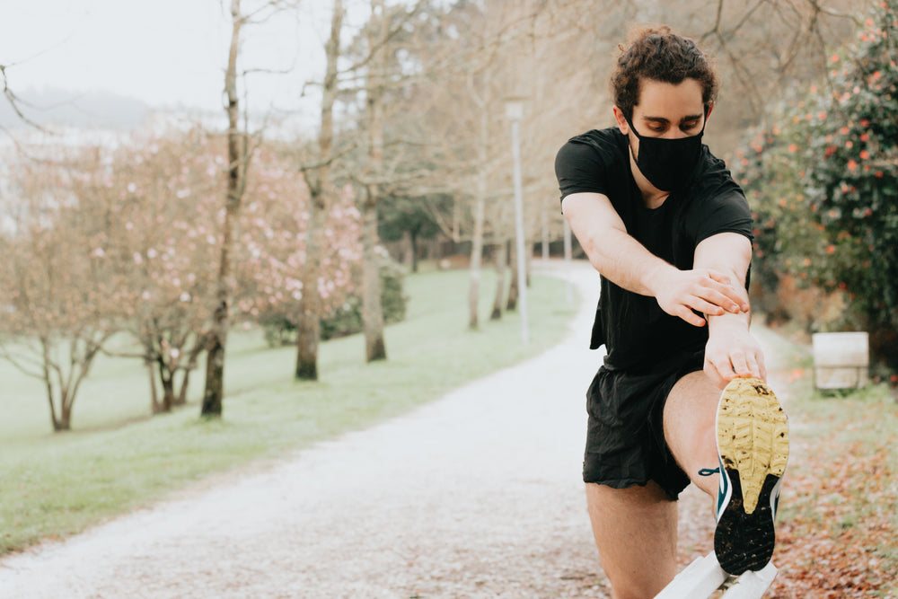 person in black face mask stretches for a run