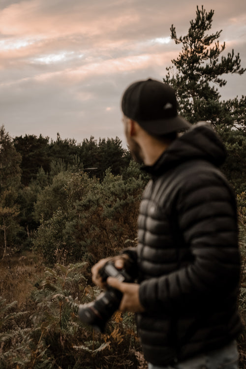 person in black holding a camera with the forest behind