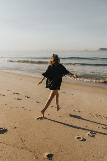 person in black walks towards the water on beach