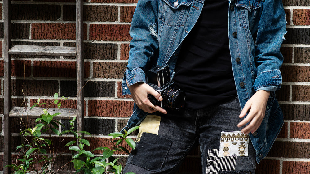 person in blue jean jacket holds camera against red brick wall