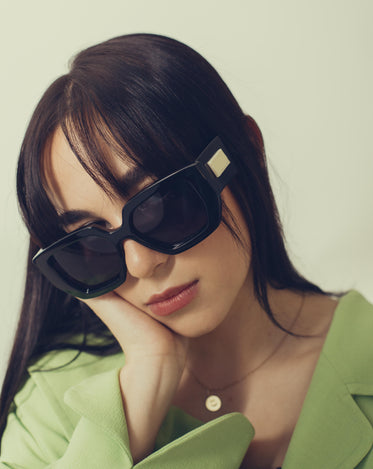 person in bold black sunglasses with hand to their cheek