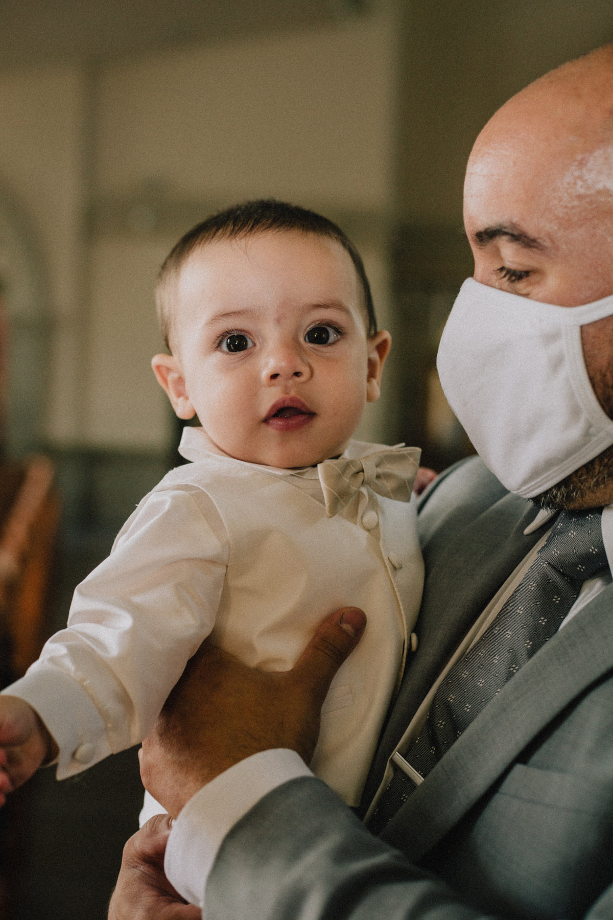 person in grey suit and facemask holds a young baby