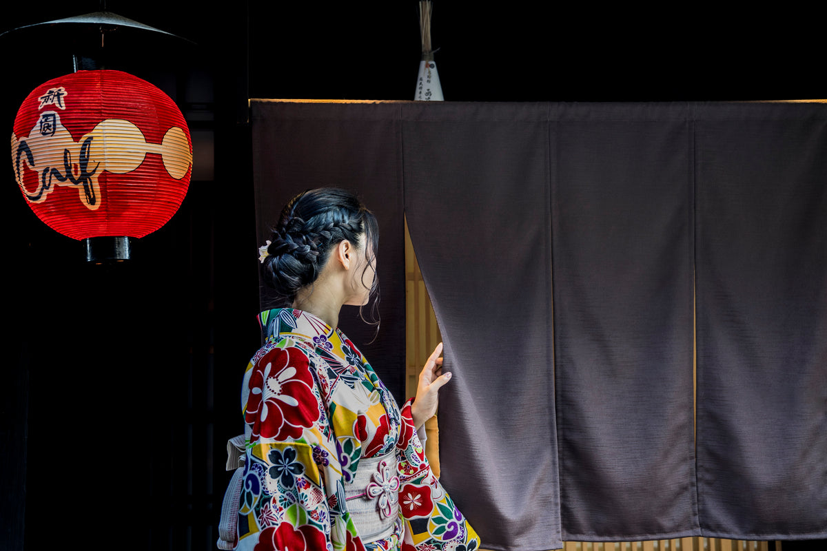 person in kimono peaks behind a black curtain