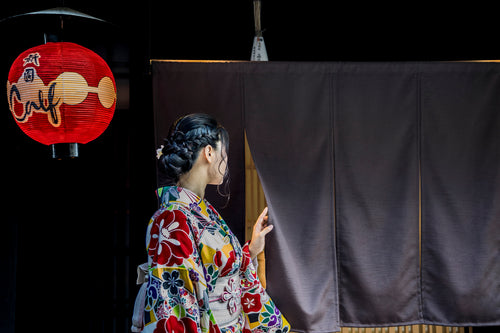 person in kimono peaks behind a black curtain