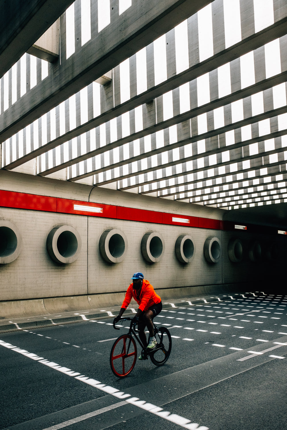 person in orange rides bike under bridge