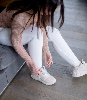 person in pink and white sits to tie their running shoes