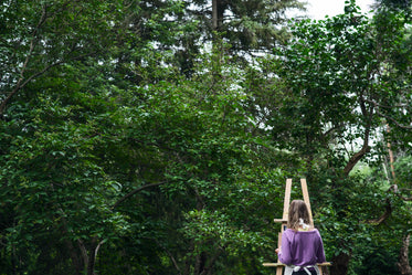 person in purple sweater paints at an easel outdoors