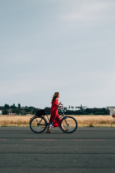person in red dress walks bicycle down the road