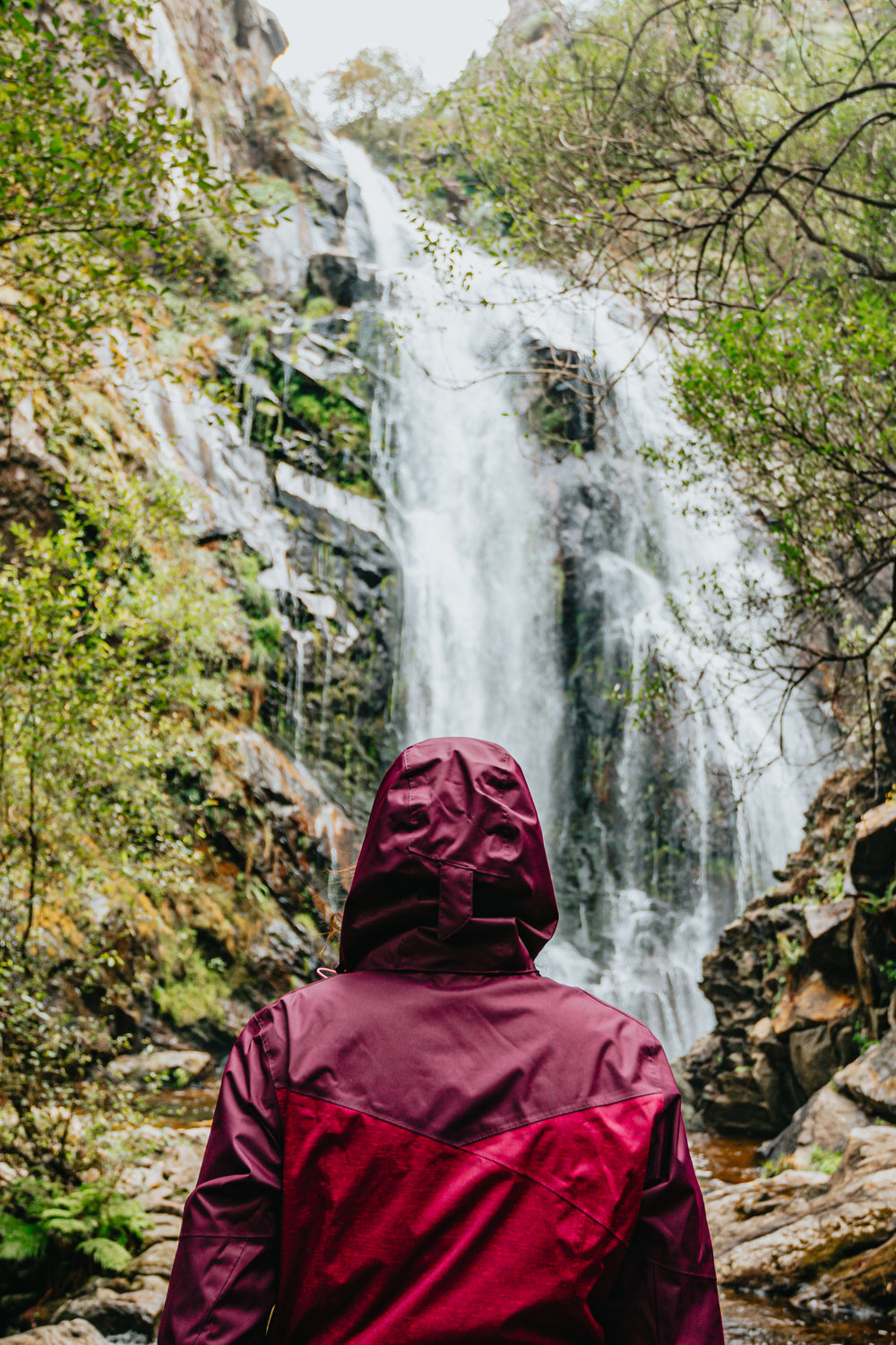 person in red raincoat admires a huge waterfall