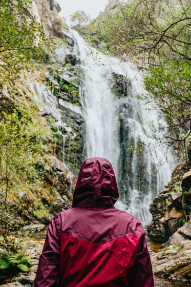 person in red raincoat admires a huge waterfall