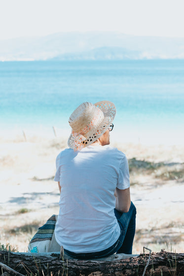 person in straw hat faces the water on a sandy beach