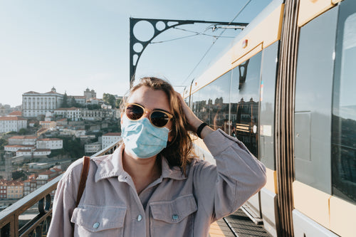 person in sunglasses and a facemask stands by a train