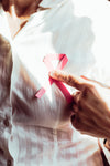 person in white holding a pink ribbon to their chest