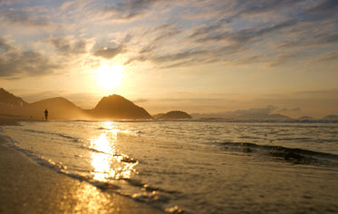 person is silhouetted walking the beach at sunrise