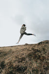 person jumps high with legs out above a brown grassy hill